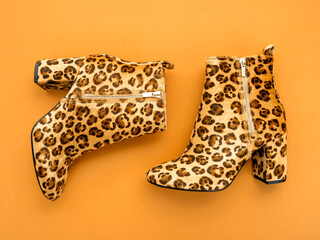 Top view shot of female boots with high heels and animal print on marigold orange backdrop. Colour trends of the year 2021. Spring summer trendy colours concept.