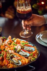People sharing Spanish dinner table with assortment of dishes. paella, octopus, whole fish, sangría and wine. Dressed for christmas