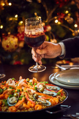 People sharing Spanish dinner table with assortment of dishes. paella, octopus, whole fish, sangría and wine. Dressed for christmas