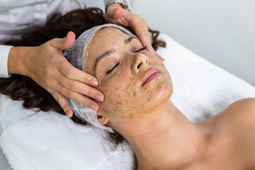 Fototapeta na wymiar Beautiful woman receiving natural green peel facial mask with rejuvenating effects in spa beauty salon.
