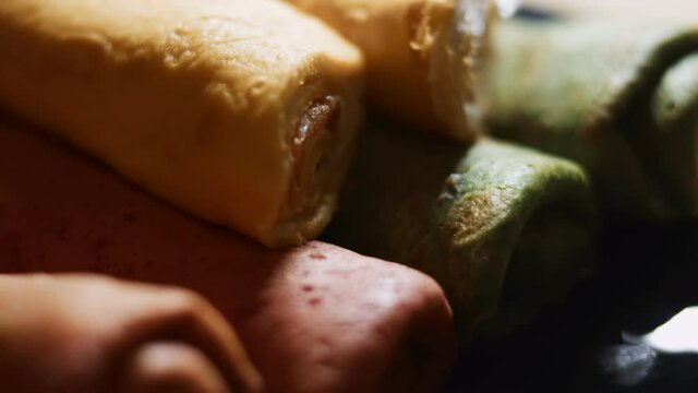 Thin tasty colorful pancakes. Macro view of red, yellow and green rolled pancakes with cream cheese and salmon filling on a dish. 4K video. Slowmotion