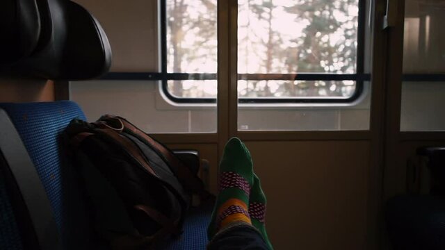 The traveler's feet lie on the couch of a train carriage in motion. Relaxation and rest on the way. Sunlight flickers down the walls.