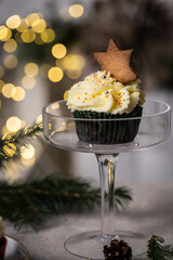 Chocolate and cherry cupcakes with mascarpone frosting and gingerbread cookies on festive table with bokeh lights on background.