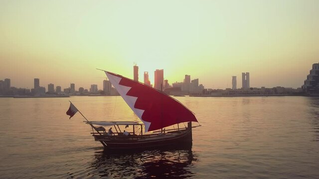 Drone view of the Traditional Arabic Dhow with Bahrain flag branded sails during the sunset time in front of Manama Skyline