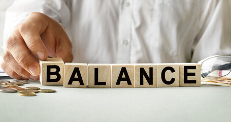 BALANCE inscription on the texture of wooden cubes. A business man holds a cube in his hand. An inscription on a financial, business or economic theme.