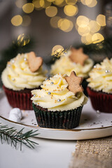 Chocolate and cherry cupcakes with mascarpone frosting and gingerbread cookies on festive table with bokeh lights on background.