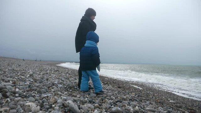 CTS1 Child Throwing Stone in Stormy Sea. Waves Crashing on Pebble Beach. Atlantic Ocean. Grey Overcast Sky. English Channel. France Europe. 2x Slow motion 60 fps 4K