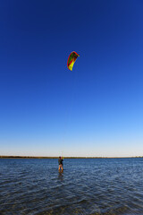 An athlete - a kitesurfer stands in shallow water, holding on to the rope of a kite that has risen into the air. Preparing to start.