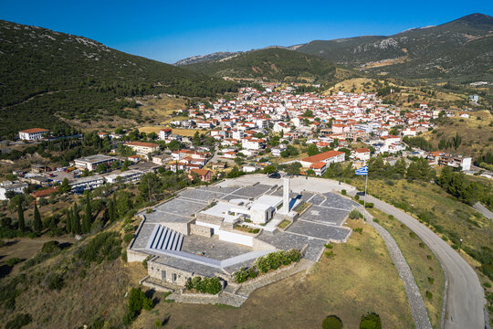 Distomo Massacre Memorial . Village Of Distomo. Sunny Day Blue Sky With Greece Flag