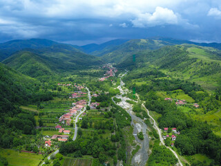 Fototapeta na wymiar Aerial drone view of Novaci village and Gilort river Valley in a stormy, cloudy day. The Parang Mountains Massif can be seen in the background covered by dark clouds. 