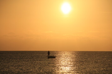 pescadero encima del bote en el atardecer , sol naranja , oceano limpio, vida acuatica, paisaje horizonte