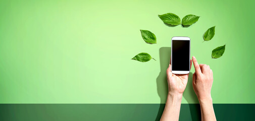 Person holding a smartphone with green leaves
