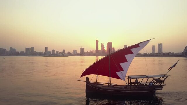 Drone view of the Traditional Arabic Dhow with Bahrain flag branded sails during the sunset time in front of Manama Skyline