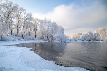 Fototapeta na wymiar Winter day on the river, partially covered with ice. On the shore there are trees in hoarfrost.