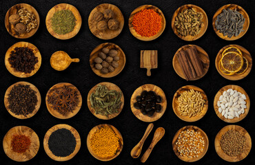 Different spices and food ingredients in wooden small plates and on a dark black background