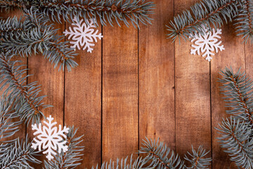 many branches of blue spruce in the form of a frame are located on a wooden surface. next to them are decorative snowflakes