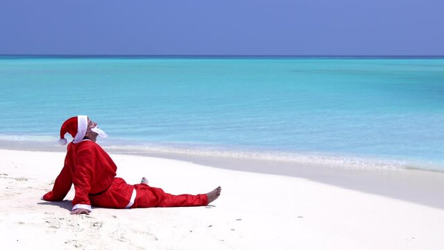 Santa Claus sitting on the beach with outstreched hands. Christmas holidays on islands