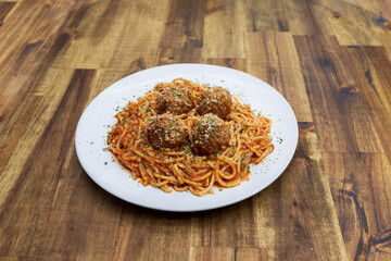 A plate of spaghetti with meat balls on a wood table at a 45 degree angle.