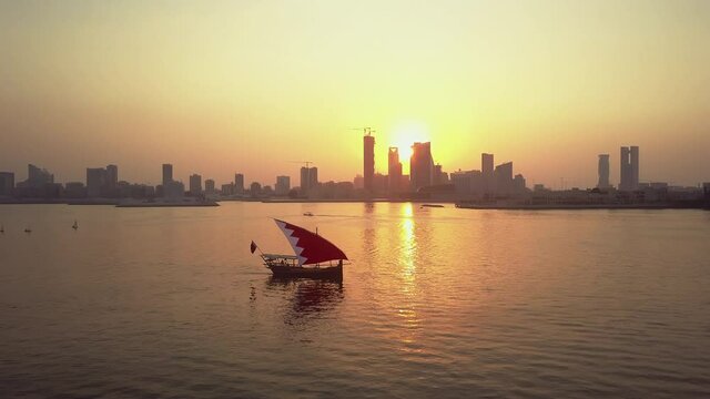 Drone view of the Traditional Arabic Dhow with Bahrain flag branded sails during the sunset time in front of Manama Skyline