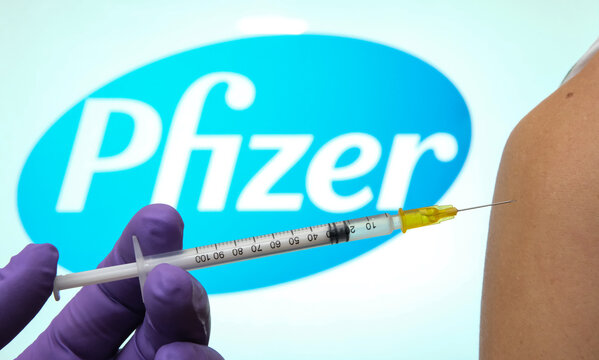 Pfizer Biontech Covid-19 vaccine concept. Hand holding a syringe against woman shoulder, with blurred Pfizer logo on the back. Real photo, not a montage. Stafford /UK - November 11 2020.