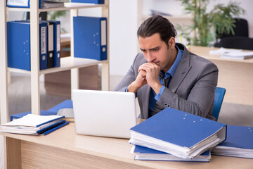 Young businessman employee unhappy with excessive work in the o