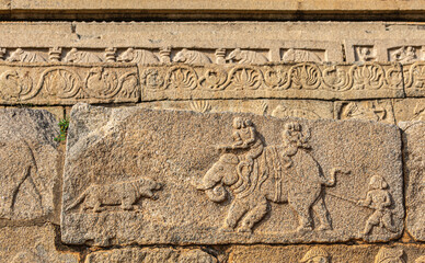Hampi, Karnataka, India - November 4, 2013: Mural sculpture on brwon stone at Royal Enclosure. Hunting scenery with hunters on elephant confronting lion.