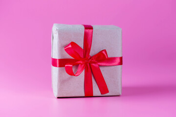 Gift wrapped in kraft paper with red ribbon on pink background