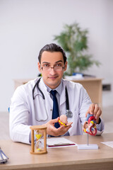 Young male doctor cardiologist in time management concept