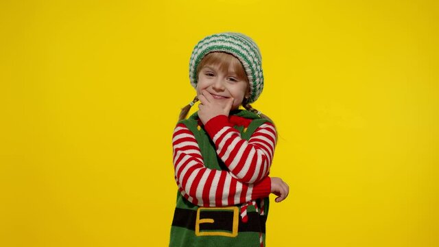 Teen kid girl in Christmas elf Santa helper costume on yellow background. Child getting present gift box, expressing amazement, extreme happiness looking inside box. New Year holidays celebration