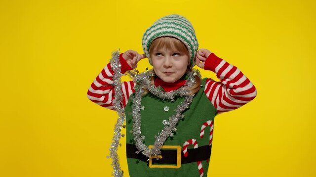 Dont want to listen. Annoyed irritated girl in Christmas elf Santa helper costume isolated on yellow background. Child covering ears, gesturing No, avoiding advice, ignoring. Unhappily, angry, sad