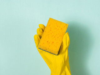 A hand in a rubber glove holds a yellow foam sponge on a blue background.
