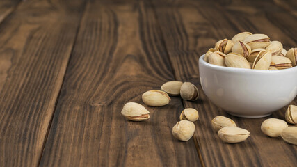 Fried pistachios in a white Cup on a wooden table.