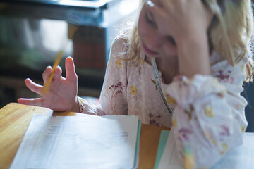 Child, holding a pencil, tries to concentrate on schoolwork at a desk.