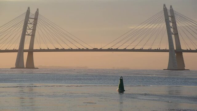 A cable-stayed bridge of Western High-Speed Diameter with traffic, over water partly covered with ice against sunset sky. Beautiful tranquil urban seascape in Saint Petersburg, Russia.
