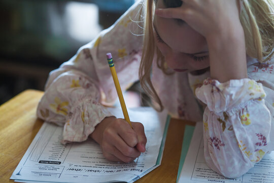 Child, holding a pencil, tries to concentrate on schoolwork at a desk.