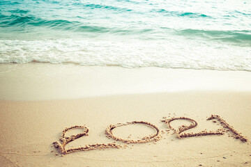 Happy New Year 2021 concept, 2021 number lettering on the sea beach, wave and golden light of sunset.