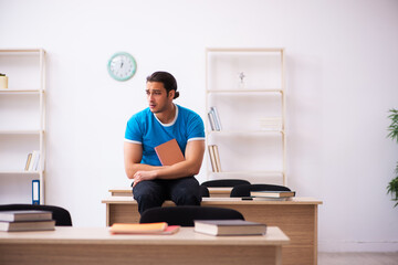 Exhausted male student preparing for the exams in the classroom