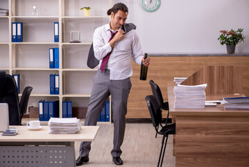 Young male employee drinking alcohol in the office