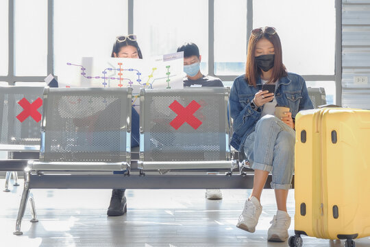 Asian young female traveler wearing face mask and sitting by following social distancing regulation with the others at public terminal station. COVID-19 awareness concept.