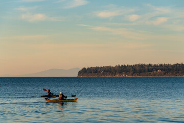 Fototapeta na wymiar Kayakers paddling in Birch Bay in the late afternoon light, peaceful scenic landscape 