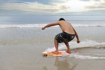 Selective focus, A young asian man is learning to ride skim board. He is turning his body to handle the balancing.