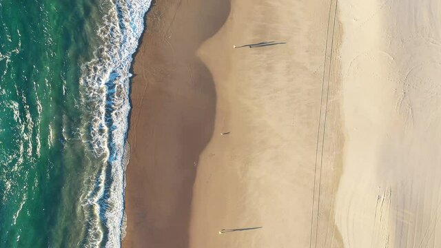 Aerial top down ascent over ocean waves on the beach at sunrise. Gold Coast, Australia