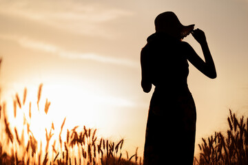 Silhouette of happy woman in wheat field at sunset