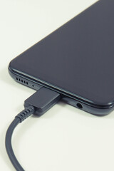 Plug of charger connected to black mobile phone. Smartphone charging