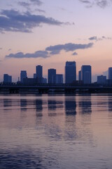 Fototapeta na wymiar 大阪淀川河川敷から梅田方面を眺める。夜明け前空がオレンジ色に輝梅田の高層ビルが水面に映る