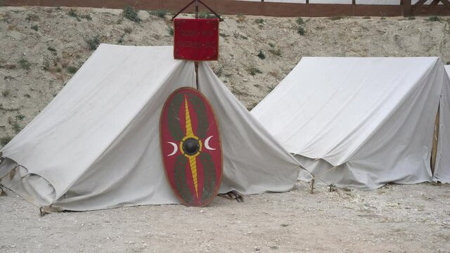 A camp of Roman Legionnaires. Vexillum (or vexilla) - military red standard by units in the Ancient Roman army. Historical Roman soldier's shield Scutum. The Roman Empire