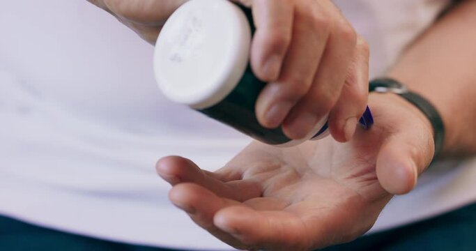 An old man empties pills from a bottle into the palm of his hand.