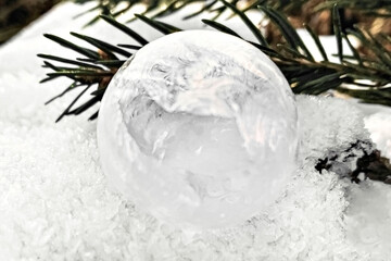 Frozen bubble with ice crystals on the snow with a spruce branch. Christmas background