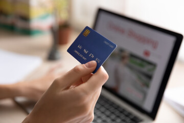 Close up woman holding plastic credit card, using laptop, paying online, young female entering information, browsing banking service, checking balance, shopping in internet, ordering goods