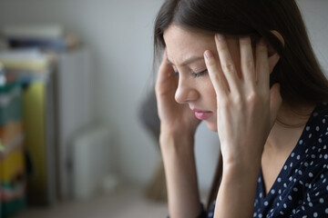 Close up unhealthy young woman suffering from strong headache or chronic migraine, touching temples with closed eyes, unhappy tired businesswoman or student feeling unwell, feeling pain